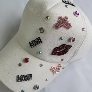 Close-up of white baseball cap with rhinestone LOVE lettering and red lip sequin patches