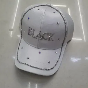 Dettaglio del cappello bianco con lettere BLACK in strass e finiture in catena lucida