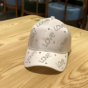 Detail of white satin baseball cap featuring shimmering rhinestone LOVE lettering on wood