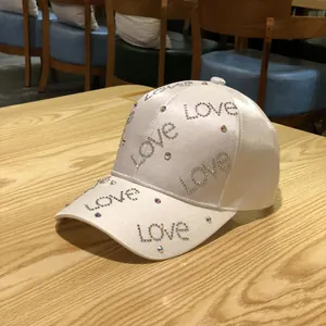 Detail of white satin baseball cap with love rhinestone lettering on a wooden table