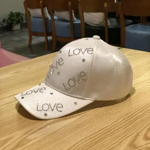 Detailed view of rhinestone Love lettering on a white satin baseball cap surface