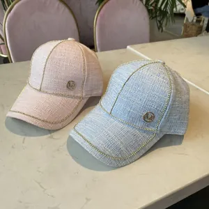 Pink and blue tweed baseball caps with gold M logo and bead chain on marble surface