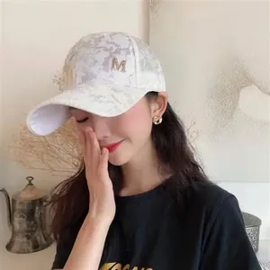 Detail shot of a grey camouflage baseball cap with a sparkling gold rhinestone M logo