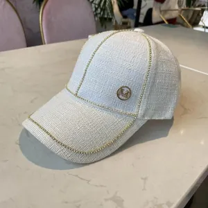 Close-up of white tweed baseball cap with golden M logo and metallic bead detailing