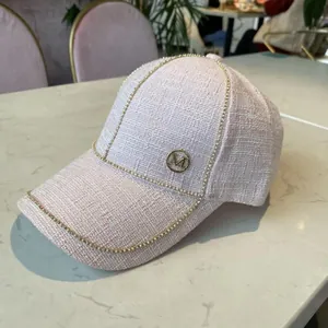 Close-up of pink tweed baseball cap featuring shiny rhinestones and a gold metal M logo