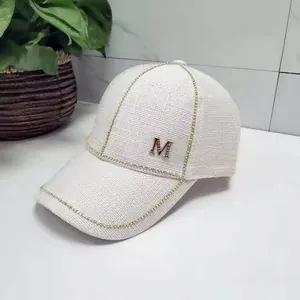 Detail of white tweed baseball cap featuring a golden M logo and sparkling rhinestone trim
