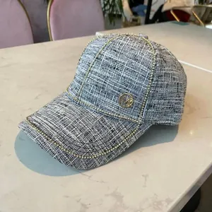Detail of tweed baseball cap with pearl trim and metal M logo on marble surface