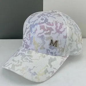 Detail of white baseball cap with colorful print and gold metal M logo on the front