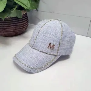 Detail of light blue tweed baseball cap featuring a gold chain trim and crystal M logo