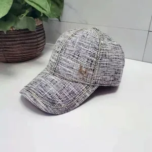 Detail of tweed baseball cap featuring black and white texture and golden M logo