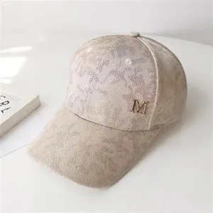 Detail shot of a beige baseball cap featuring a floral pattern and a metal M letter logo