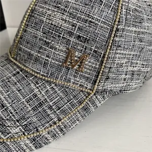 Detail of grey tweed baseball cap with gold crystal M logo and metallic chain trim