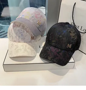 Close-up of textured camouflage baseball caps featuring a metallic gold M logo on the side