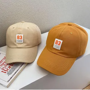 Detail view of beige and yellow baseball caps with number 83 patch on white display