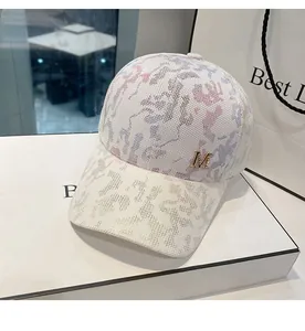 Detail of white mesh baseball cap with watercolor print and golden metal M logo