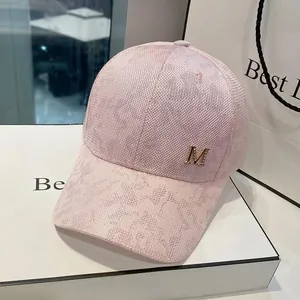 Detail of pink baseball cap featuring a metallic gold M logo and textured mesh fabric