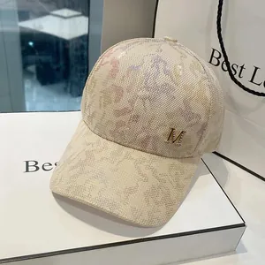 Close-up of beige printed baseball cap featuring a metallic M logo and abstract pattern