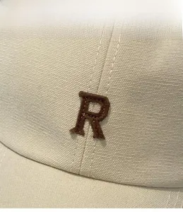 Détail d'une casquette beige en sergé de coton avec broderie du logo R en daim