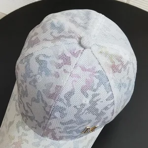 Macro view of white baseball cap with colorful camo patterns and golden M metal logo