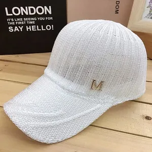 Detail of white knit mesh baseball cap featuring a golden M logo on wood surface