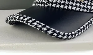 Gros plan du tissu pied-de-poule et de la visière en cuir noir avec logo doré élégant