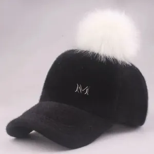 Detail der schwarzen Plüsch-Basecap mit weißem Kunstfell-Bommel und Metall M Logo