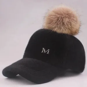 Detail einer schwarzen Fleece-Baseballkappe mit braunem Kunstpelz-Bommel und Metall-M-Logo