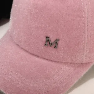 Detailaufnahme der rosa Plüsch-Basecap mit flauschiger Textur und silbernem Metall-M-Logo