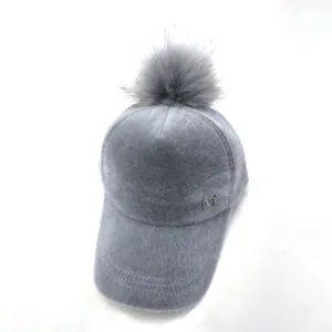 Detail der grauen Plüsch-Basecap mit flauschigem Bommel und Metall-M-Logo