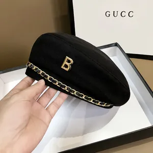 Detailaufnahme einer schwarzen Baskenmütze mit goldenem B-Logo und modischer Metallkette