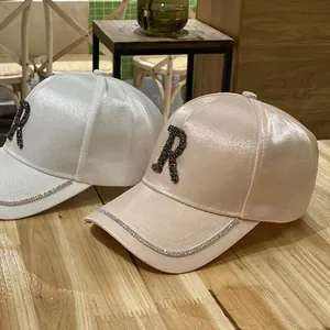 Detail of satin baseball caps with rhinestone letter R and crystal-trimmed brim decoration