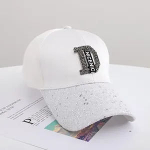 Detail of white baseball cap showing rhinestone D logo and silver sequins on the brim