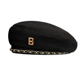 Klassische schwarze Wollbaske mit goldenem B-Logo und dekorativer Metallkette