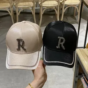 Detail of satin baseball caps in beige and black featuring rhinestone R logos