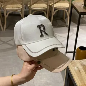 Detailed view of rhinestone R letter and shimmering silk texture on white baseball cap