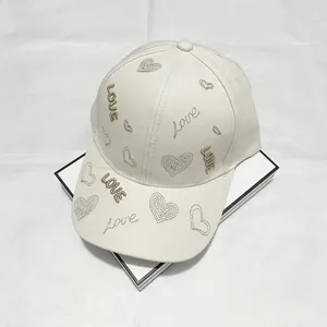Dettaglio del cappello beige con ricami a cuore e scritte LOVE in filo dorato elegante