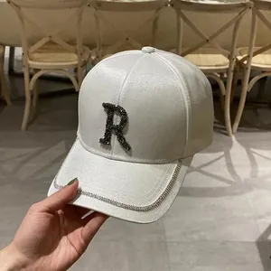 Detail of white satin baseball cap with rhinestone letter R and sparkling brim