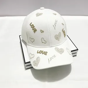 Dettaglio del cappellino in cotone bianco con ricamo LOVE dorato e motivi a cuore