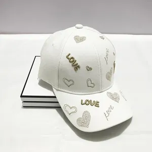 Dettaglio del cappellino bianco in tela con ricamo a cuore dorato e scritta LOVE