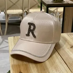 Detailed macro view of champagne silk baseball cap with rhinestone letter R and silver trim
