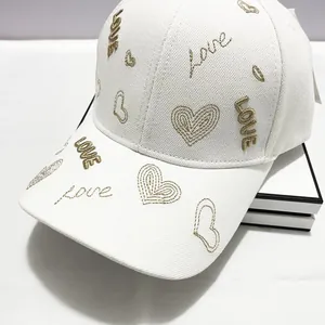Dettaglio ravvicinato del ricamo dorato a cuore e LOVE su un cappello bianco in twill