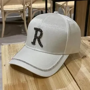 Detailed view of white satin baseball cap with rhinestone letter R and diamond edge brim