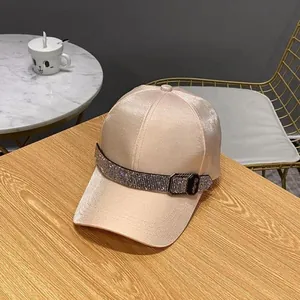 Detailed view of champagne satin baseball cap featuring rhinestone buckle on wood table