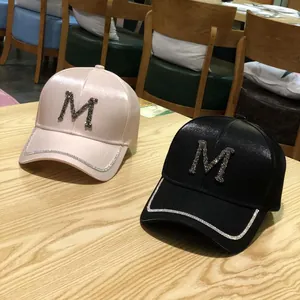 Detailed view of pink and black satin baseball caps featuring rhinestone M letter patterns