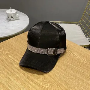 Detail of black satin baseball cap with rhinestone band and metal buckle on wooden surface