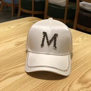 Close-up of white satin baseball cap with rhinestone letter M and sparkling brim edges