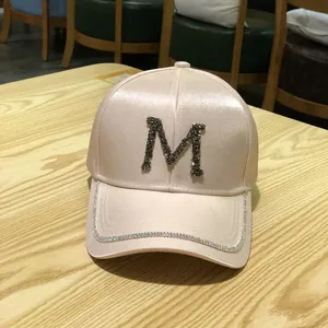 Detailed shot of champagne satin baseball cap with rhinestone M letter and diamond brim