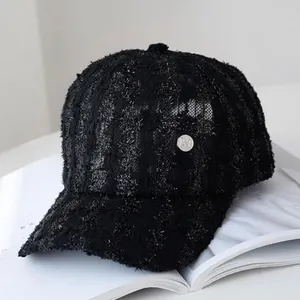 Detail of black tweed baseball cap with silver metallic M badge and woven texture