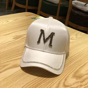 Close-up of white satin baseball cap with rhinestone M letter and diamond-edged brim