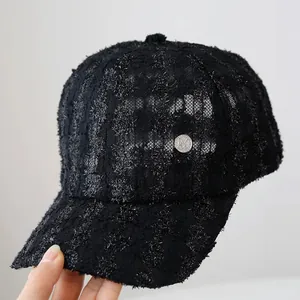 Detail of black lace baseball cap featuring a silver metallic M emblem and tweed texture